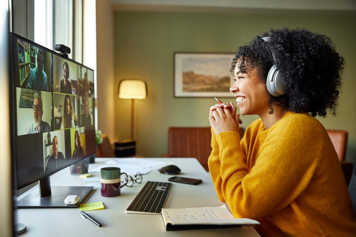 a woman smiling at her computer screen with her headphones on participating in a group work meeting